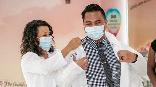 Photo of Dr. Carmela Sosa giving physician white lab coat to new pediatric resident