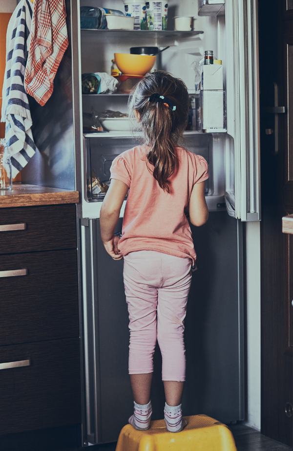 Young girl standing on stool and looking into a refrigerator